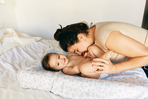 Madre haciendo cosquillas a su bebé sobre el cambiador. - solucionesbanohub.compaña - 1