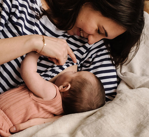 Una mamá y su bebé felices estiradas en la cama mientras le da el pecho - solucionesbanohub.compaña - 1