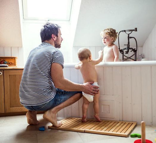 Un papá a punto de dar un baño relajante a sus dos hijos, uno de ellos todavía bebé, con productos para la higiene Mustela - solucionesbanohub.compaña - 1