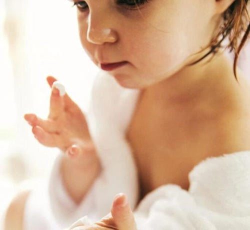 Una bebé recién bañada y con albornoz se aplica crema Mustela en la cara - solucionesbanohub.compaña - 1