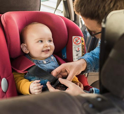 Un bebé contento sentado en la sillita del coche mientras su papá le abrocha el cinturón de seguridad - solucionesbanohub.compaña - 1