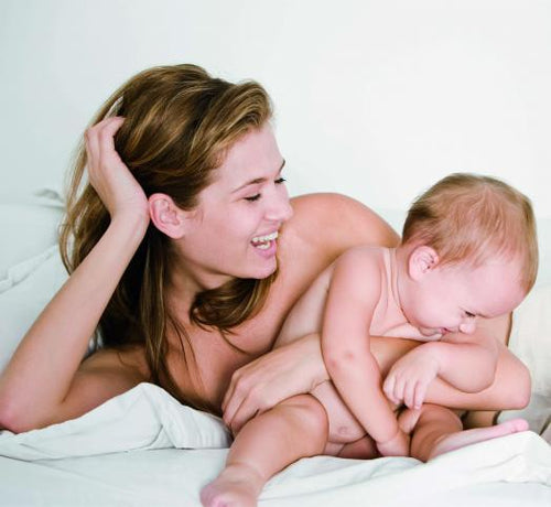 Una mamá y su bebé felices estiradas en la cama después de un baño relajante con jabón Mustela - solucionesbanohub.compaña - 1