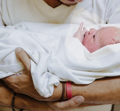 Papá cogiendo a su bebé recién nacido sobre una toalla blanca. - solucionesbanohub.compaña - 1