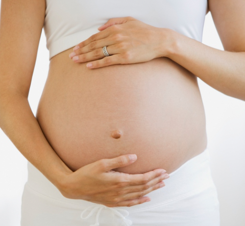 Plano de una tripa de una mamá vestida con pantalon blanco y toop blanco mientras abraza su tripa con las manos. - solucionesbanohub.compaña - 1