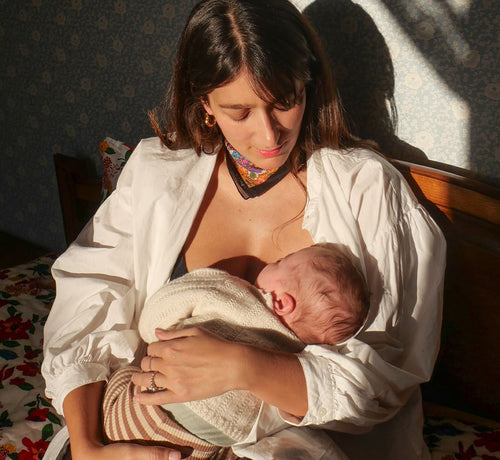 Madre amamantando a su bebe sentada sobre una cama - solucionesbanohub.compaña - 1