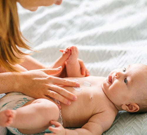 Una mamá aplicando una crema emoliente a su bebé con piel atópica. - solucionesbanohub.compaña - 1