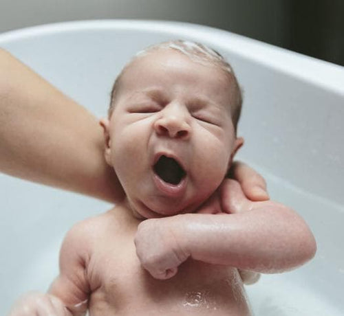 Un bebé en los brazos de su mamá mientras recibe un baño de espuma con productos Mustela - solucionesbanohub.compaña - 1