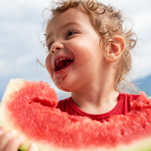 Una niña pequeña comiéndose una raja de sandia  - solucionesbanohub.compaña - 1