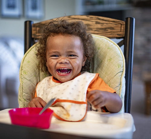 Niña sentada en una silla comedor riéndose.  - solucionesbanohub.compaña - 1