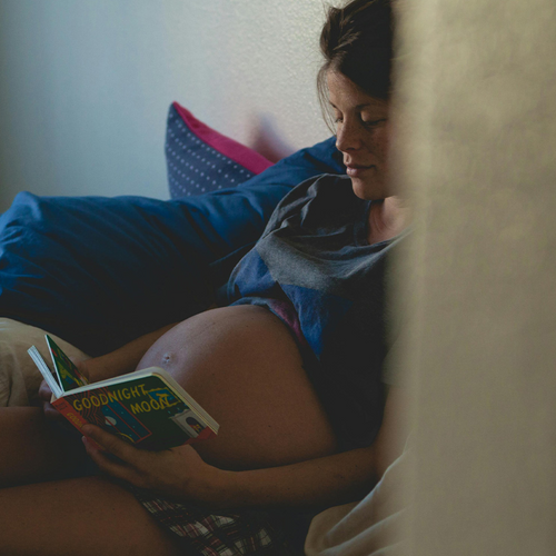 Mujer embarazada sentada en un sillón mientras ve un libro para bebés. - solucionesbanohub.compaña - 1