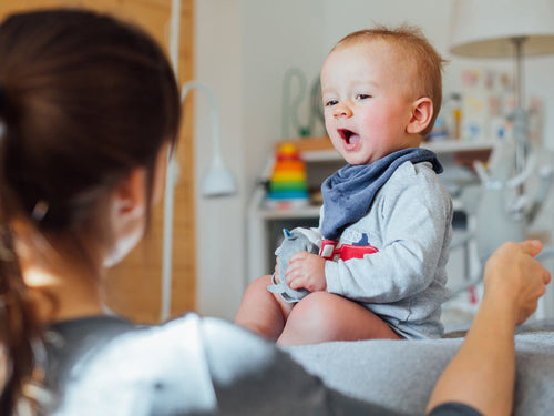 Una mamá de espaldas con su bebé que se encentra sentado y con la boca abierta para hablar. - solucionesbanohub.compaña - 1