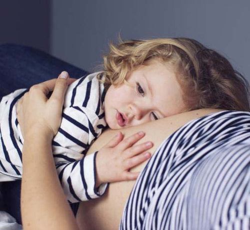 Una bebé abraza el vientre de su madre embarazada mientras las dos están estiradas en la cama - solucionesbanohub.compaña - 1