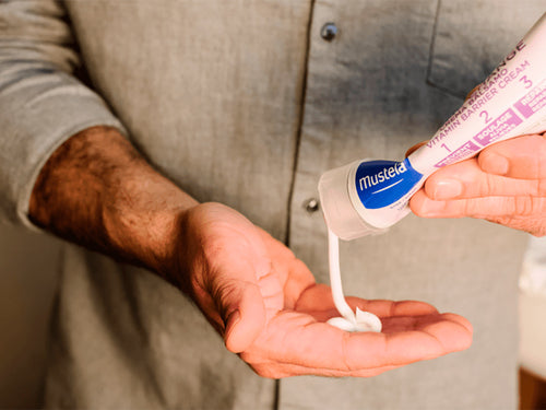 Un papá se dosifica en la mano la crema bálsamo 123 de Mustela para picores y rojeces antes de aplicarlo en la zona del pañal de su bebé - solucionesbanohub.compaña - 7
